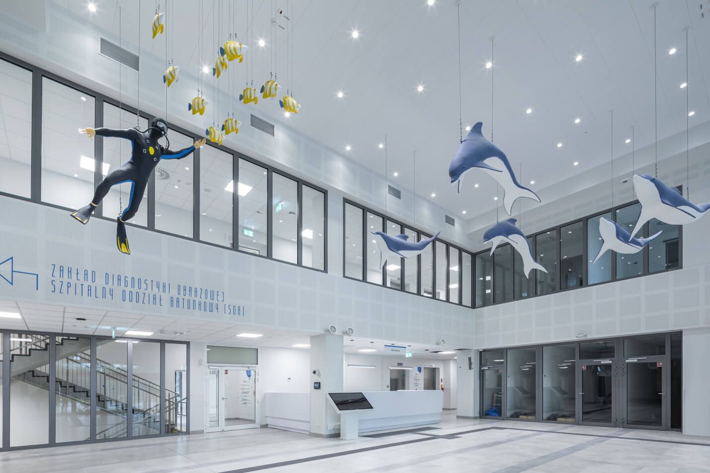 A bright, modern hospital interior featuring a reception area, suspended decorations in the shape of fish, dolphins and a diver, and modern LED lighting | Lumedic