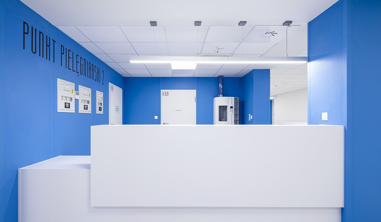 A blue and white reception area with a white desk in a healthcare facility, featuring appropriate medical lighting