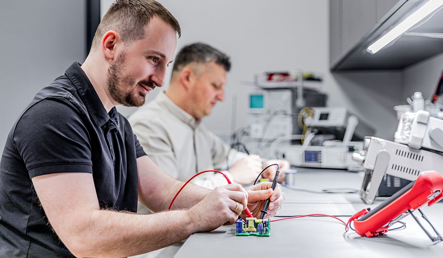 Two technicians in an electronics laboratory, carrying out precision assembly tasks under suitable lighting conditions