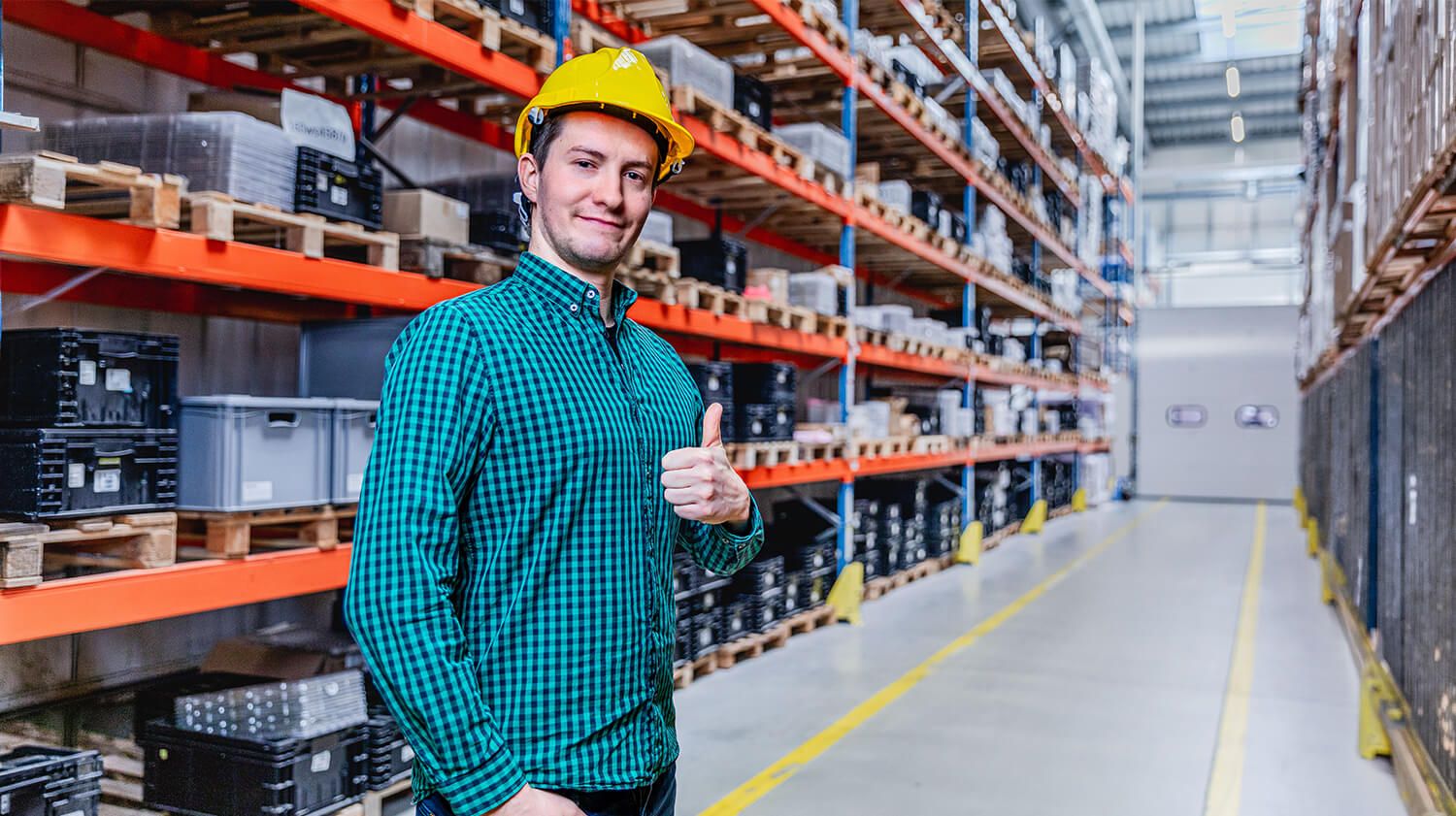 A smiling warehouse worker giving a thumbs-up highlights the importance of good lighting for comfort and productivity at work.